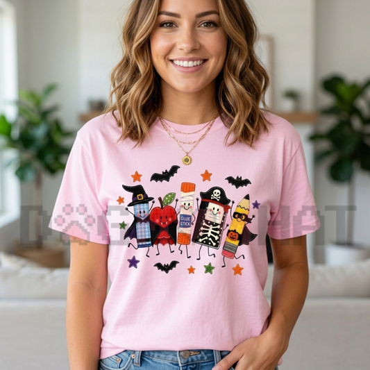 Front view of the Halloween Teacher T-Shirt displaying spooky smiling school supplies and witch hat graphics printed across the chest. - dogmomhat